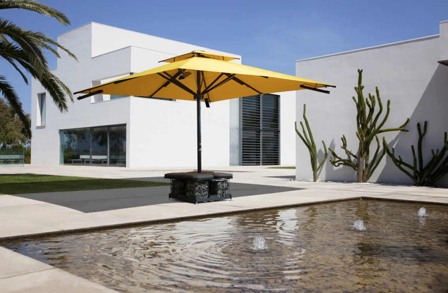 Moderner Außenbereich mit gelbem Sonnenschirm und Wasserbrunnen vor einem weißen Gebäude